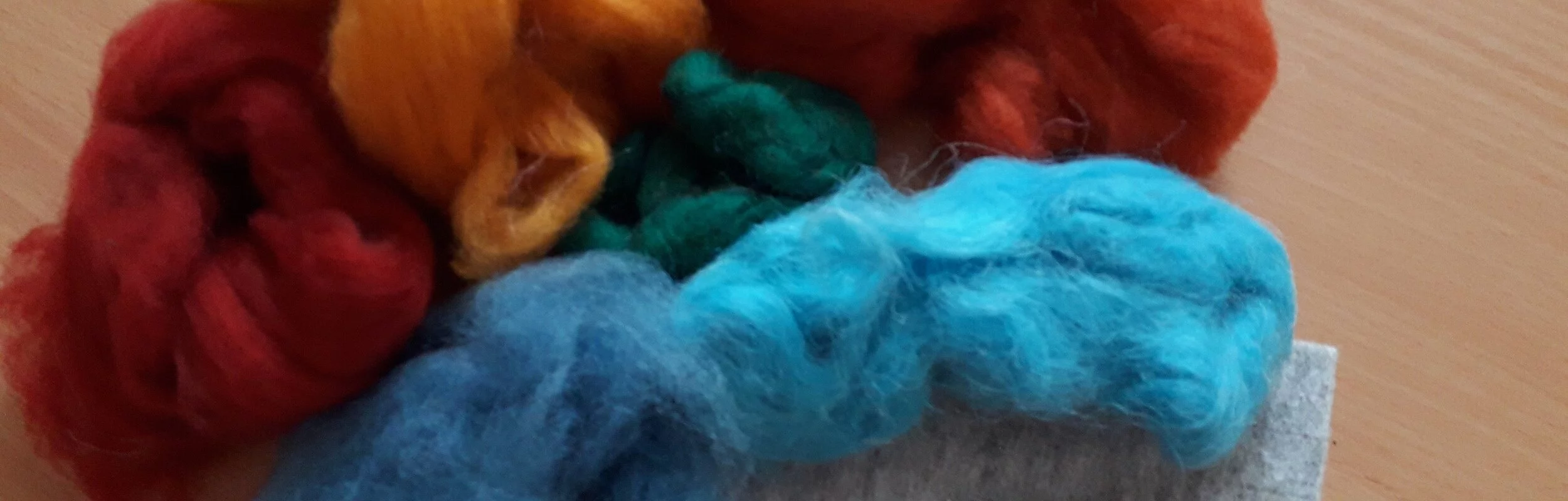 Bunte Filzwolle und Filznadeln auf einem Tisch.