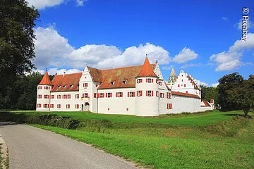 Jagdschloss Grünau Das Schloss mit seinen roten Fensterläden und roten Dächern inmitten grüner Wiesen.