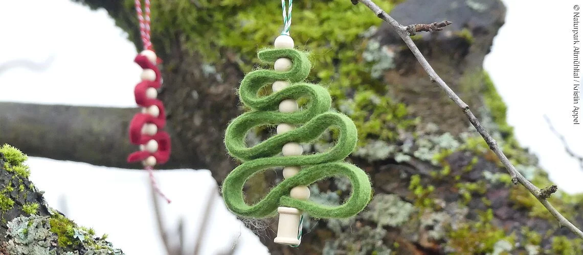 Ein roter und grüner Filz-Anhänger in Form eines Christbaumes hängen draußen an einem Baum.