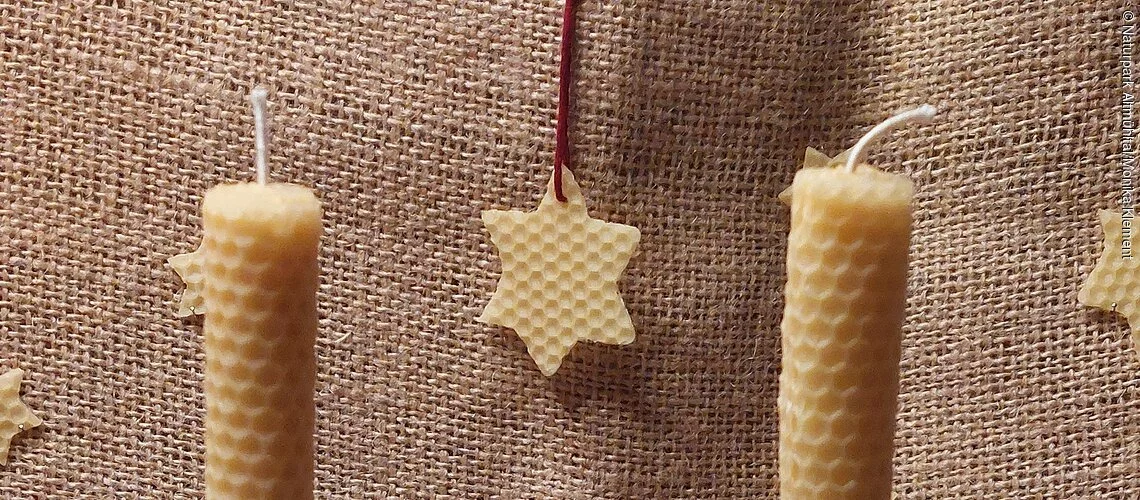 2 selbstgemachte Bienenwachskerzen weihnachtlich dekoriert mit Zapfen und Walnüssen, im Hintergrund Sternanhänger aus Bienenwachs