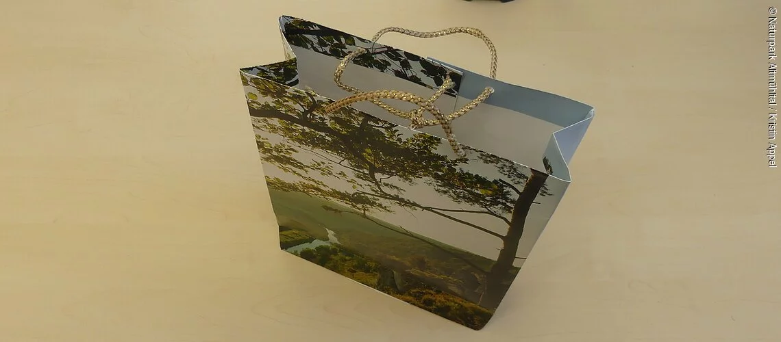 Auf einem Tisch steht eine Geschenktüte, die aus alten Kalenderblätter gefaltet wurde.