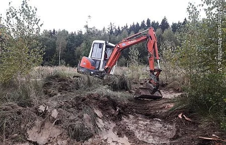 Roter Bagger gräbt Loch in Erdboden