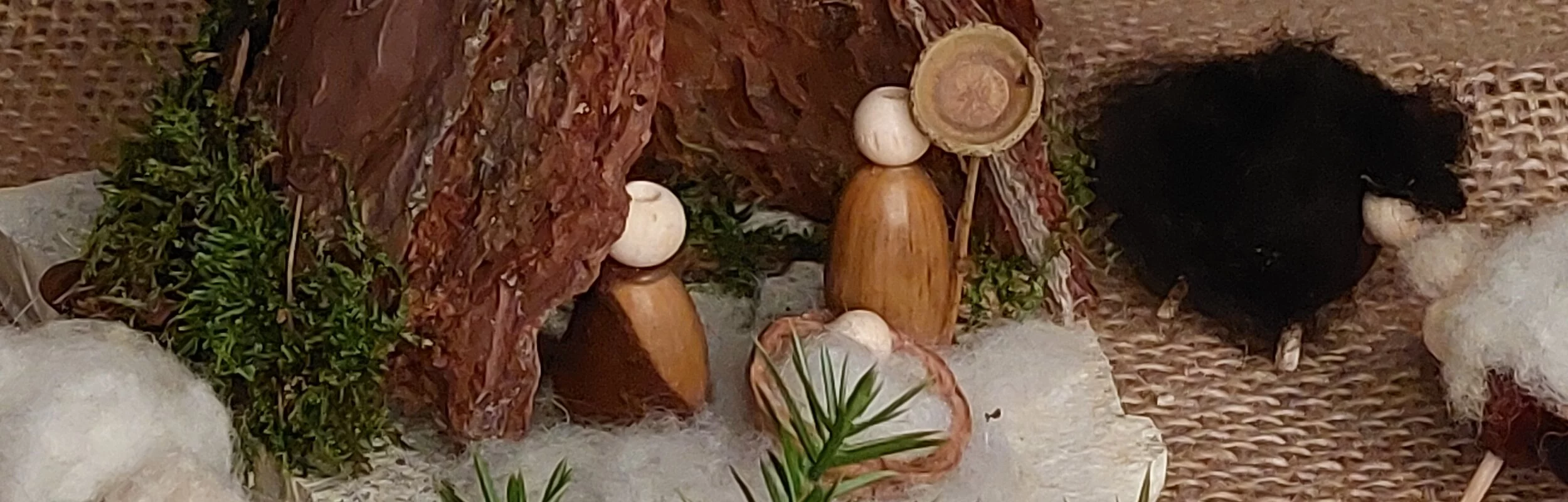 Auf einer weihnachtlich dekorierter Decke steht eine kleine Krippe aus Rinde und Naturstein. Die Krippenfiguren sind aus Eicheln gestaltet.
