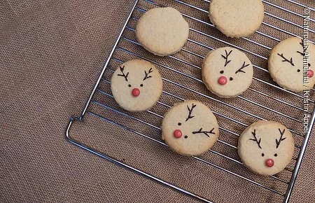 Rudolf Plätzchen Rudolf Plätzchen liegen auf einem Ofengitter (Helle, runde Butterplätzchen mit roter Smartie-Nase und Schokoladen-Augen und -Geweih). Fünf Plätzchen sind dekoriert und zwei noch nicht.
