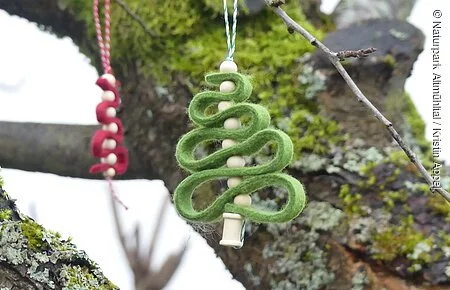 Filz-Christbaumschmuck Ein roter und grüner Filz-Anhänger in Form eines Christbaumes hängen draußen an einem Baum.
