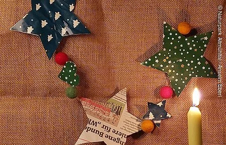 Weihnachtsgirlande Weihnachtsgirlande mit Papiersternen und Filzkugeln, davor eine brennende Kerze