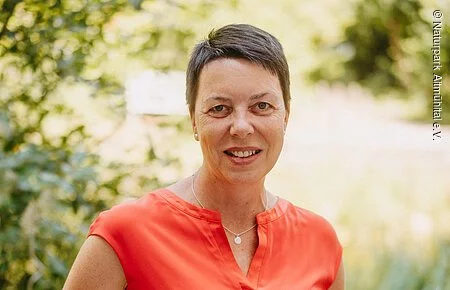 Christina Ziegler Frau mit orangen Oberteil vor grünem Hintergrund
