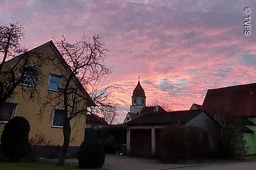 Ein lila-oragener Horizont über Häusern und einem Kirchturm.