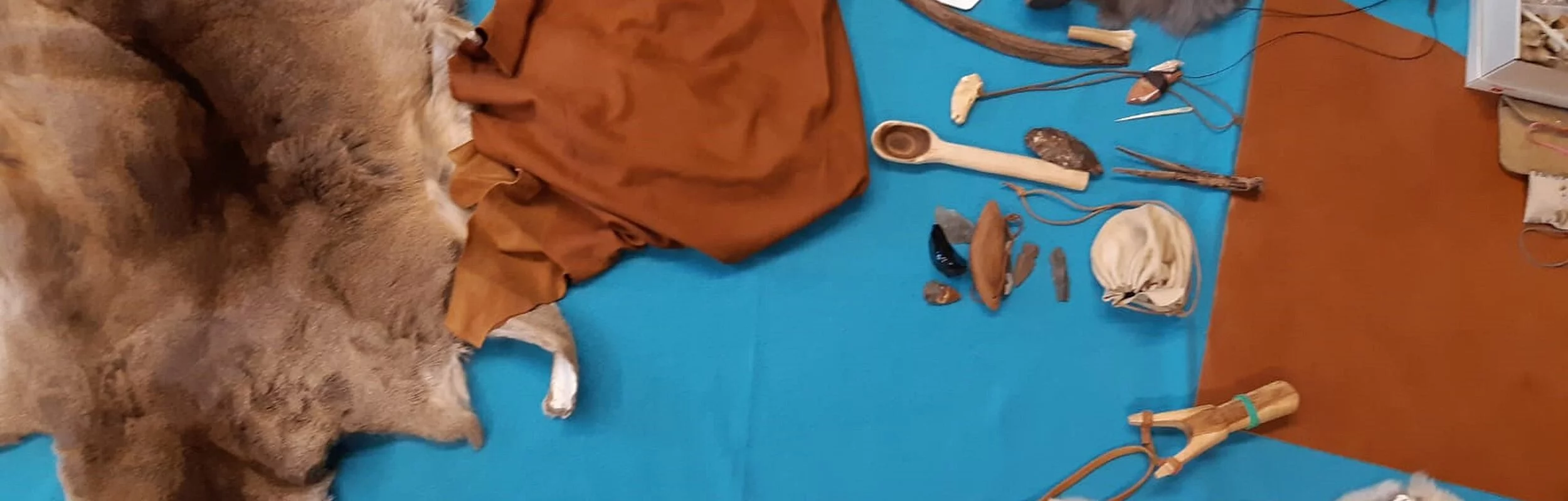 Blaues Tuch, auf dem mehrere Geräte und Gegenstände liegen: Fell, Kuhhorn, Lederstücke, Holzstücke, Knochen