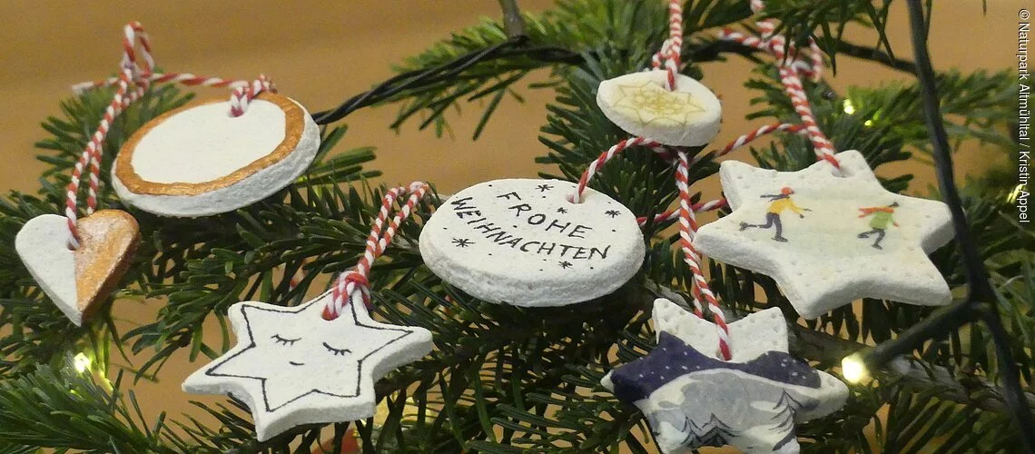 Einige weihnachtlich dekorierte Salzteig-Anhänger liegen auf einem Tannenzweig.