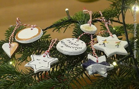 Salzteig-Anhänger Einige weihnachtlich dekorierte Salzteig-Anhänger liegen auf einem Tannenzweig.