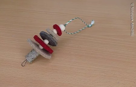 Filz-Weihnachtsbaum Ein Weihnachtsbaum-Anhänger aus rotem und grauem Filz liegt auf einem Holztisch