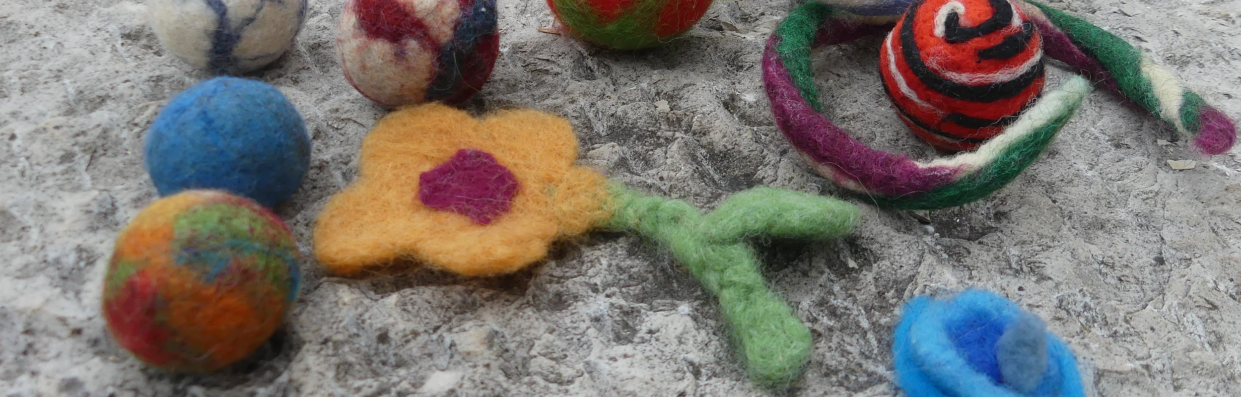 gefilzte Kugeln und eine Filzblume liegen auf einer Mauer.