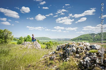 Blick vom Bubenheimer Berg Frau sitzt auf einem Stein in Yogapose im Vordergrund ein Felsen