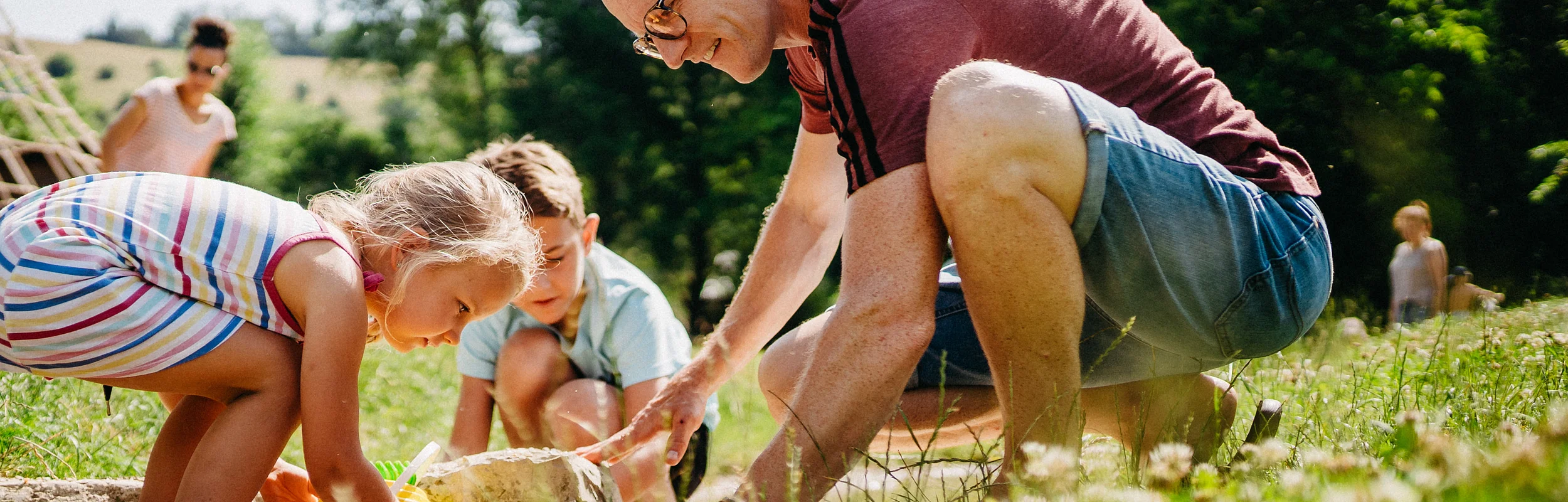 Ein Vater spielt mit zwei Kinder – einem Mädchen und einem Jungen – in einem flachen Bachlauf.
