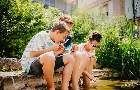 Umweltbildung im Biotopgarten Familie sitzt am Teich und untersucht das Gewässer