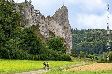 Zwei Rennradler fahren unterhalb des massiven Burgsteinfelsen gen Dollnstein