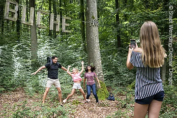 Eine Familie macht ein Foto mit einer Buche, einer Station im Walderlebnispfad.