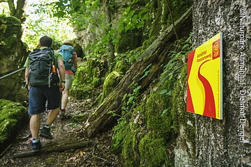 Die Klamm bei Riedenburg am Altmühltal-Panoramaweg Im Vordergrund hängt ein Wanderschild des Altmühltal-Panoramaweges. Ein Wanderpärchen steigt die Treppen der Riedenburger Klamm hinauf.