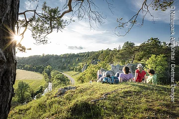 Vier Wanderer liegen im grünen auf den 12 Aposteln am Altmühltal-Panoramaweg. Sie genießen den Sonnenuntergang und den Blick ins Tal.