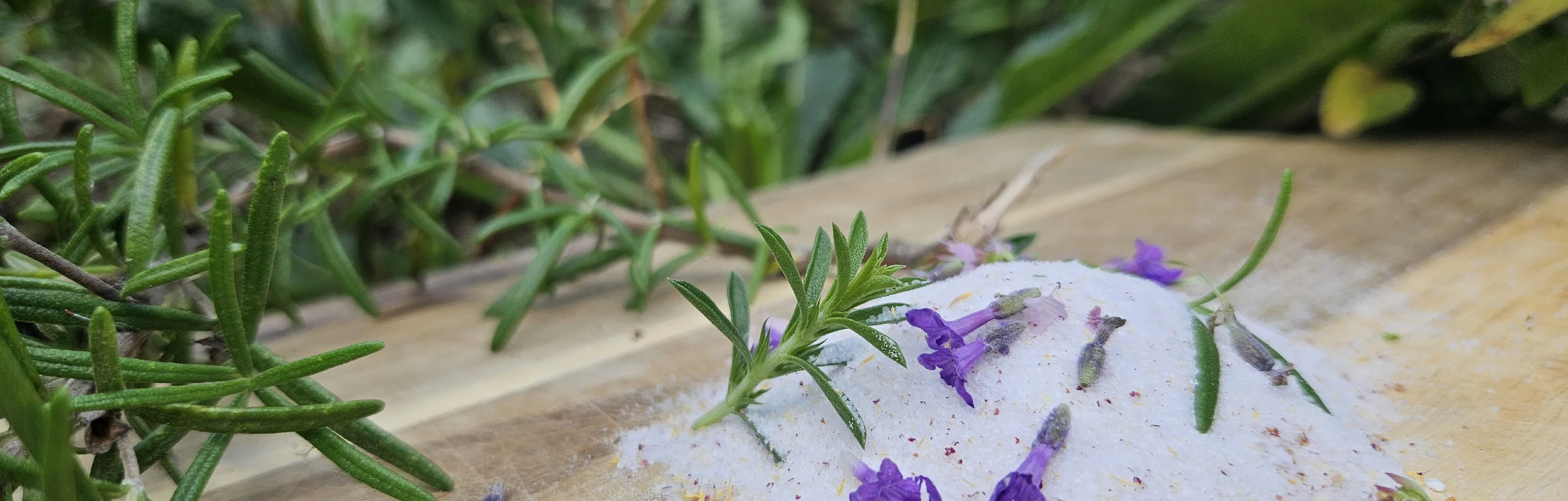 Auf einem Holzbrett liegt ein Häufchen Salz mit Lavendelblüten und einem Rosmarinzweig