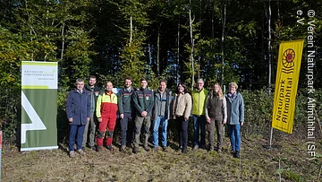 Gruppenfoto "Waldzukunft Naturpark Altmühltal" Personengruppe vor Bäumen, gelbe Fahne mit Ammonit, grün-weiße Fahne mit Baum