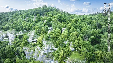 Dichte bewaldete Hügel mit zwei kleinen Gebäuden auf einem Felsvorsprung.