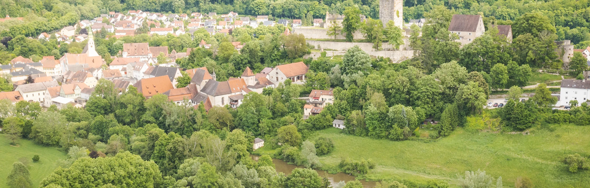 Luftaufnahme eines Dorfes mit Kirche, Burg und Wohnmobilen auf einem Campingplatz am Fluss.