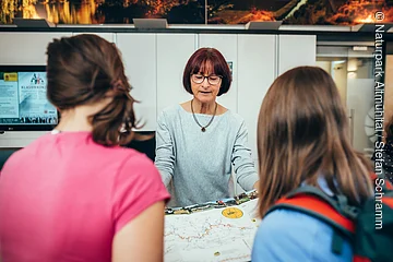 Frau zeigt zwei Personen eine Landkarte in einem Informationsbüro.