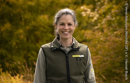 Weibliche Person vor grün-gelben Bäumen im Hintergrund