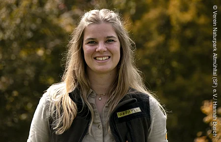 Weibliche Person  vor grün-gelben Bäumen im Hintergrund