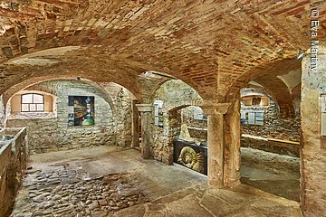 Historischer Kellerraum mit gewölbter Decke aus Backstein und Ausstellungsstücken an den Steinwänden.