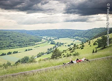 Der Altmühltaler-Panoramaweg an der langen Bank bei Obereichstätt Zwei Wanderinnen liegen auf einer langen Holzbank und schauen ins weitläufige grüne Altmühltal.
