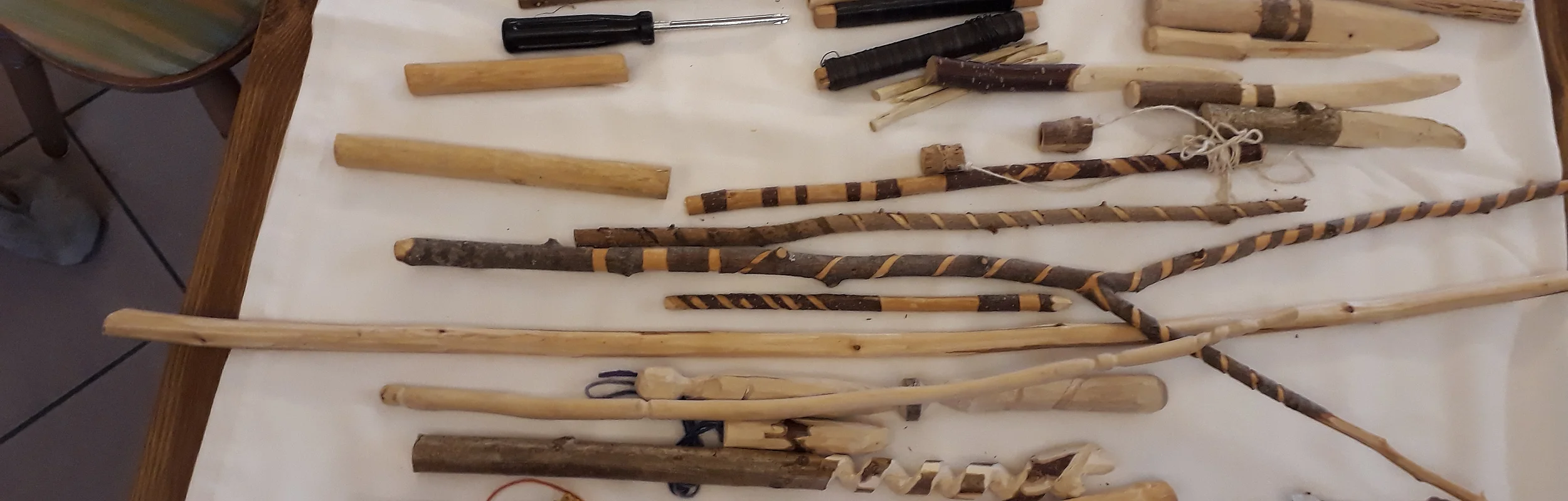 Auf einem Tisch liegen verschiedene geschnitzte Holzobjekte: u.a Messer, Flöte, Zauberstab, uvm.