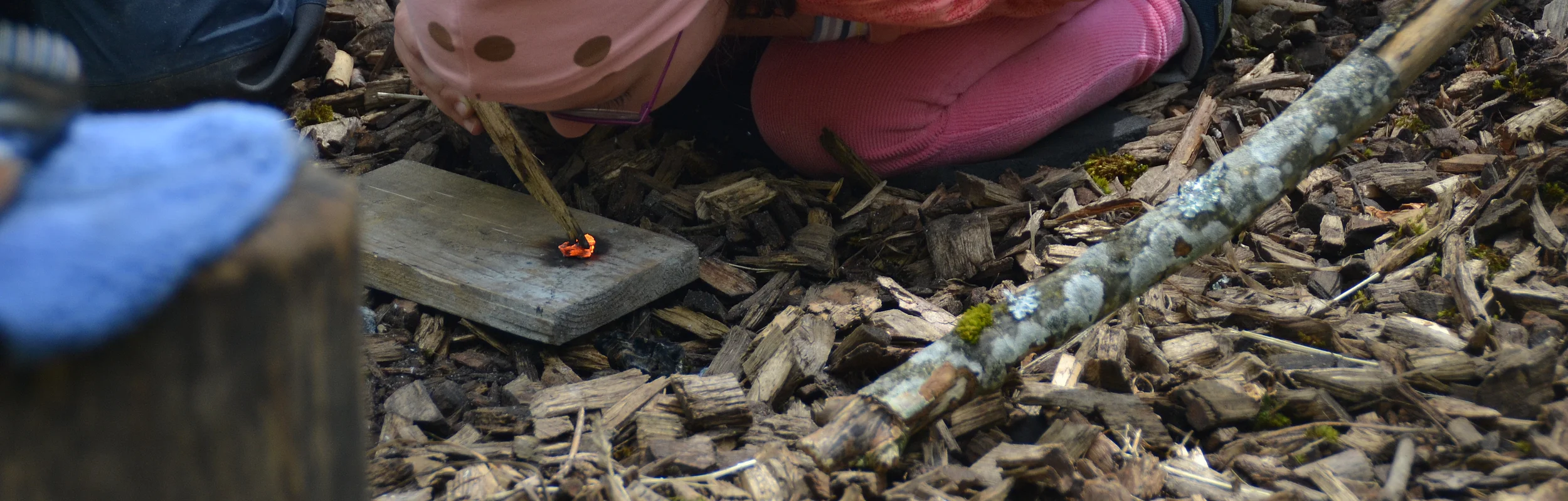 In Kind kniet am Boden und pustet auf ein glimmendes Stück Holz