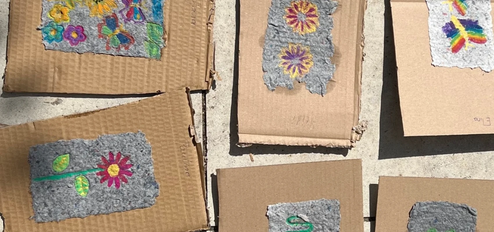 Mehrere Hand geschöpfte Papierstücke mit Blumen- und Schmetterlingsmotiven liegen auf braunen Kartonstücken auf einem Steinboden.