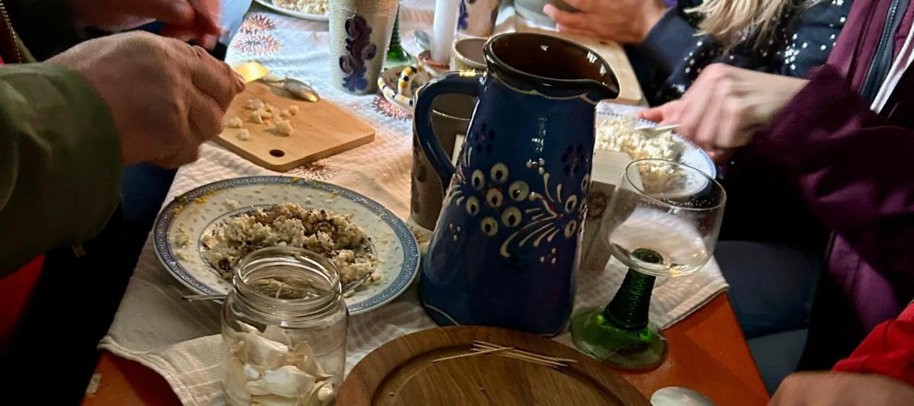 Menschen bereiten an einem gedeckten Tisch mit Kerze und Keramikgeschirr Speisen zu.