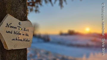 Kraftorte rund um Nassenfels Schild mit der Aufschrift „Nimm Dir Zeit und blicke in die schöne Natur“ an einem Baum im Winter bei Sonnenuntergang.