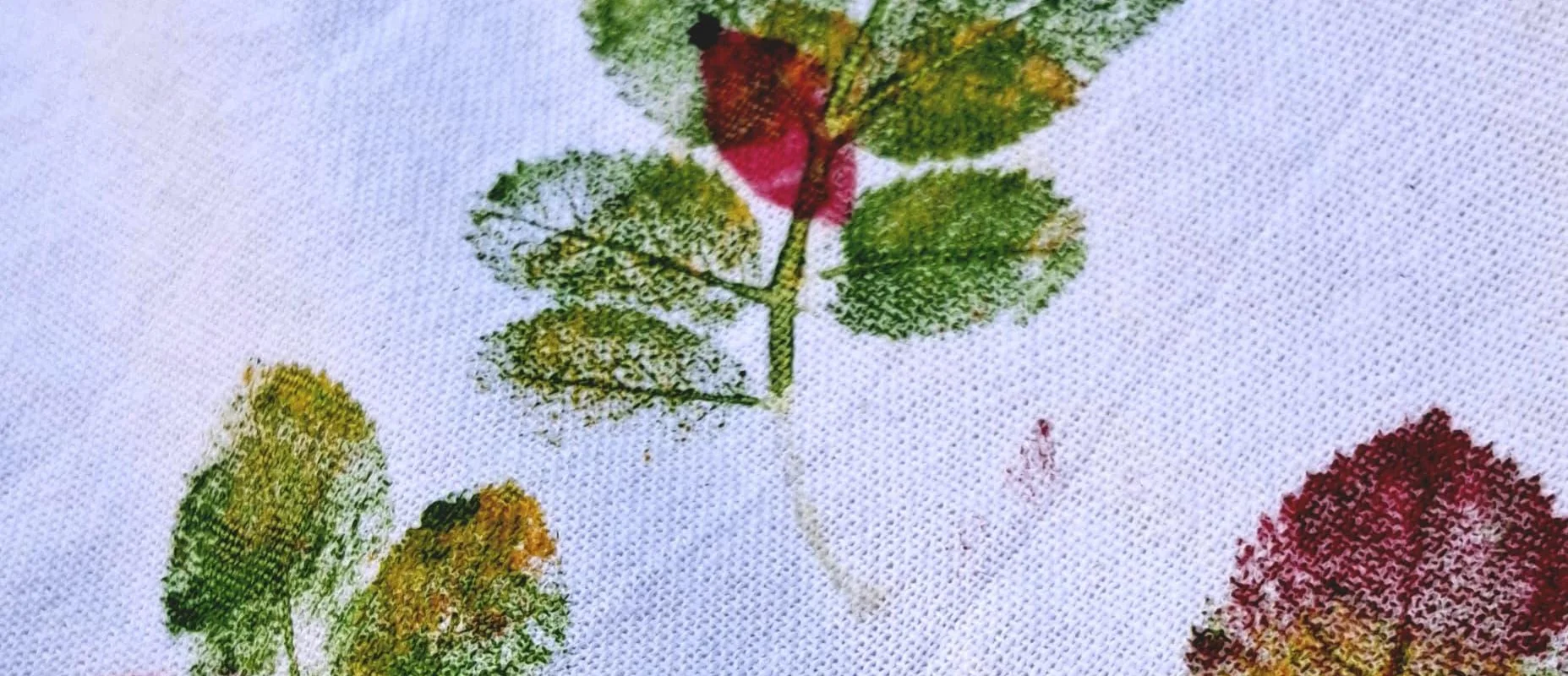 Druck von grünen und roten Blättern auf weißem Stoff mit sichtbarer Textur