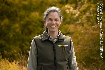 Weibliche Person vor grün-gelben Bäumen im Hintergrund