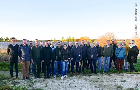 Gruppenfoto von 20 Personen vor einem Solarfeld bei klarem Himmel und herbstlicher Vegetation im Hintergrund.