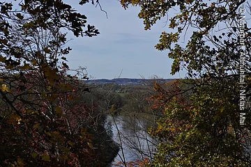Fluss fließt durch herbstlichen Wald mit bunten Blättern unter blauem Himmel.