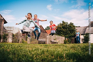 Drei Kinder springen über ein Seil im Garten, zwei weitere halten das Seil gespannt.