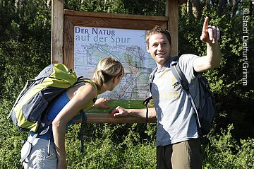 Wandertafel Der Natur auf der Spur Zwei Wanderer stehen vor einer Tafel vom Wanderweg - Der Natur auf der Spur –