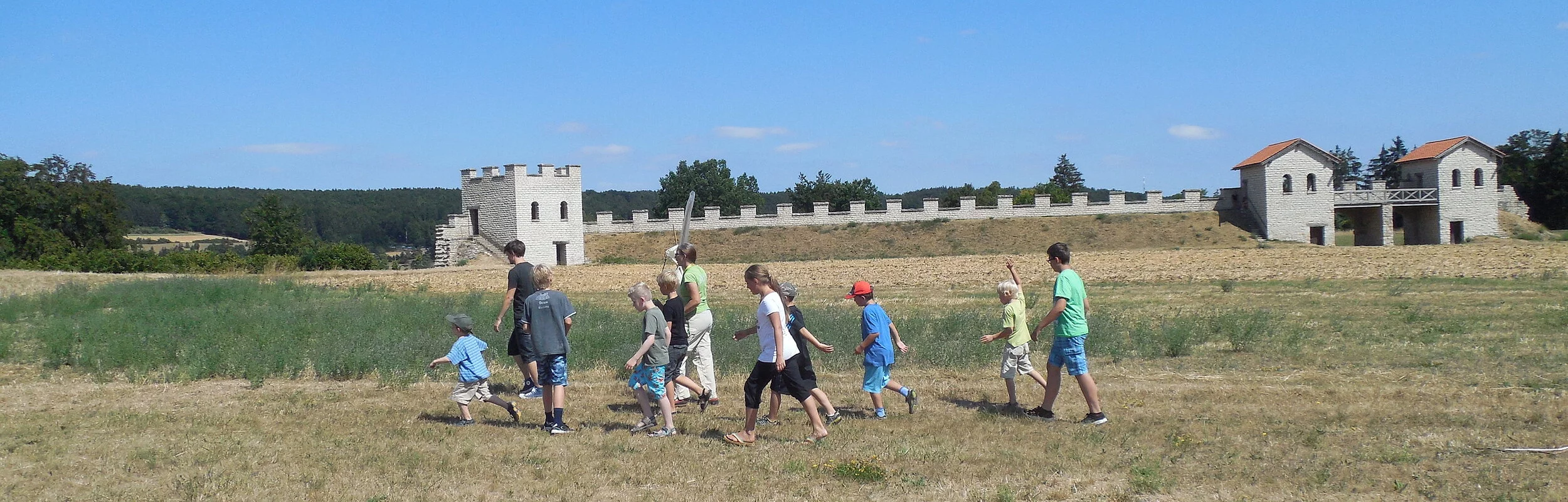 Blick von Süden über die Wiese auf das Nordtor, davor laufende Kindergruppe
